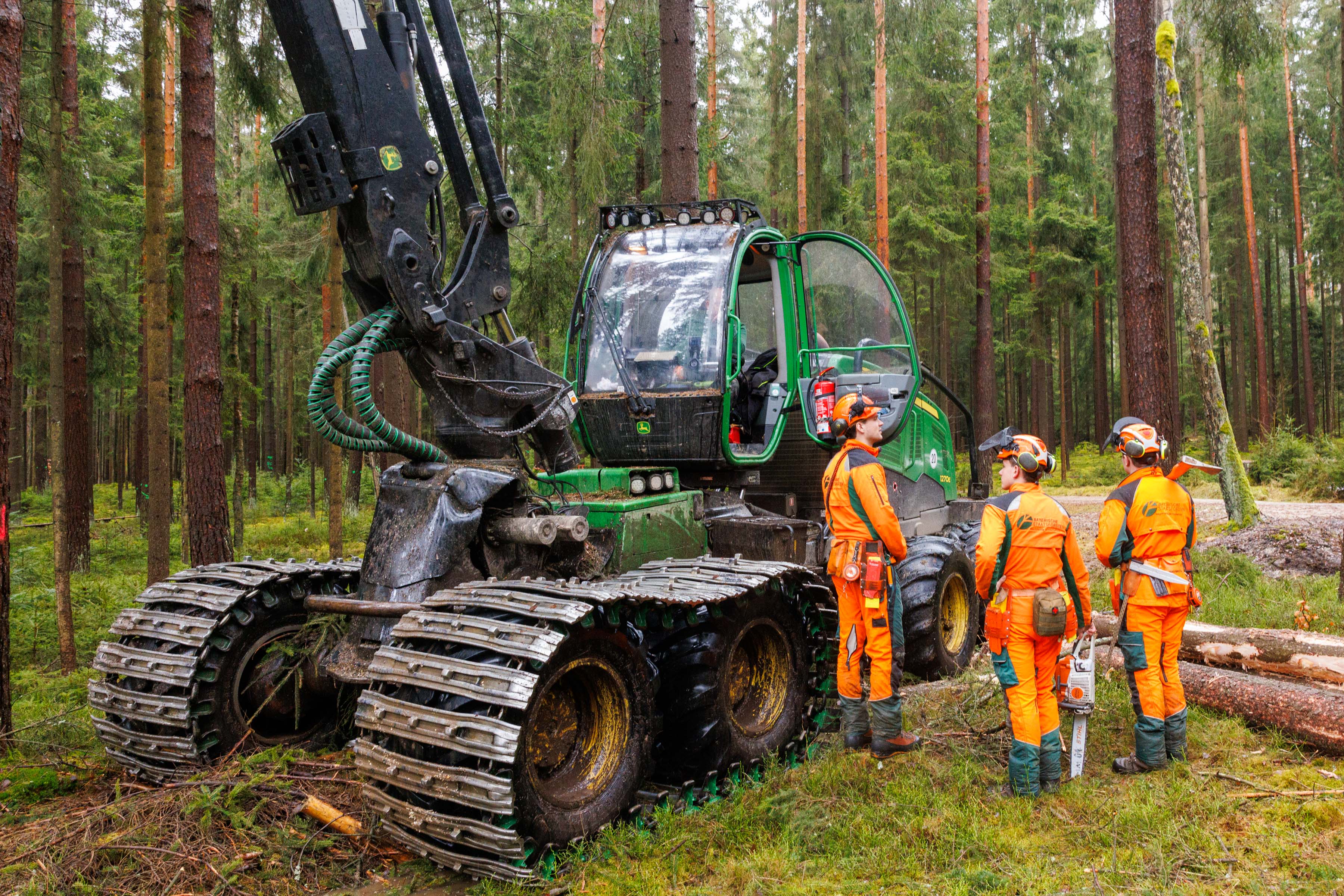 Forstwirt stehen vor einem Harvester und besprechen das weitere Vorgehen bei der Holzernte.