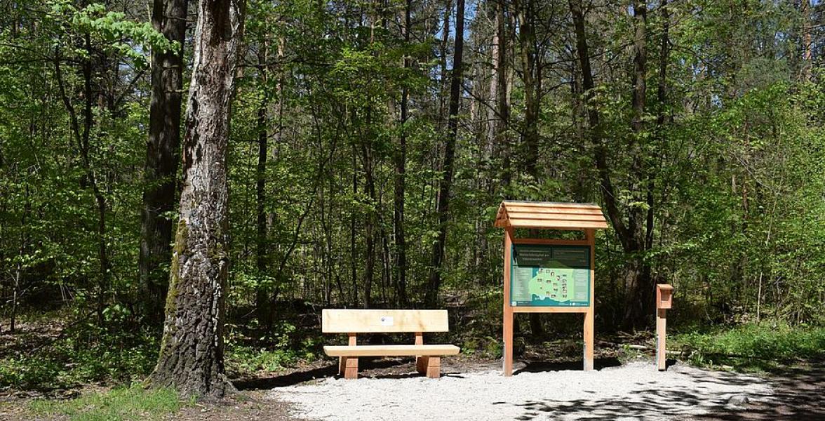 Infotafel steht neben Bank im Wald