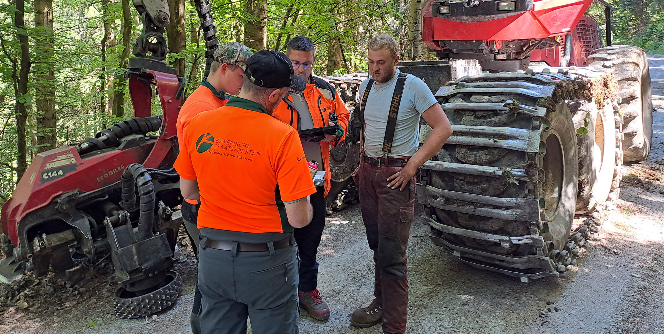 Forstarbeiter besprechen den nächsten Einsatz, im Hintergrund steht eine Holzerntemaschine