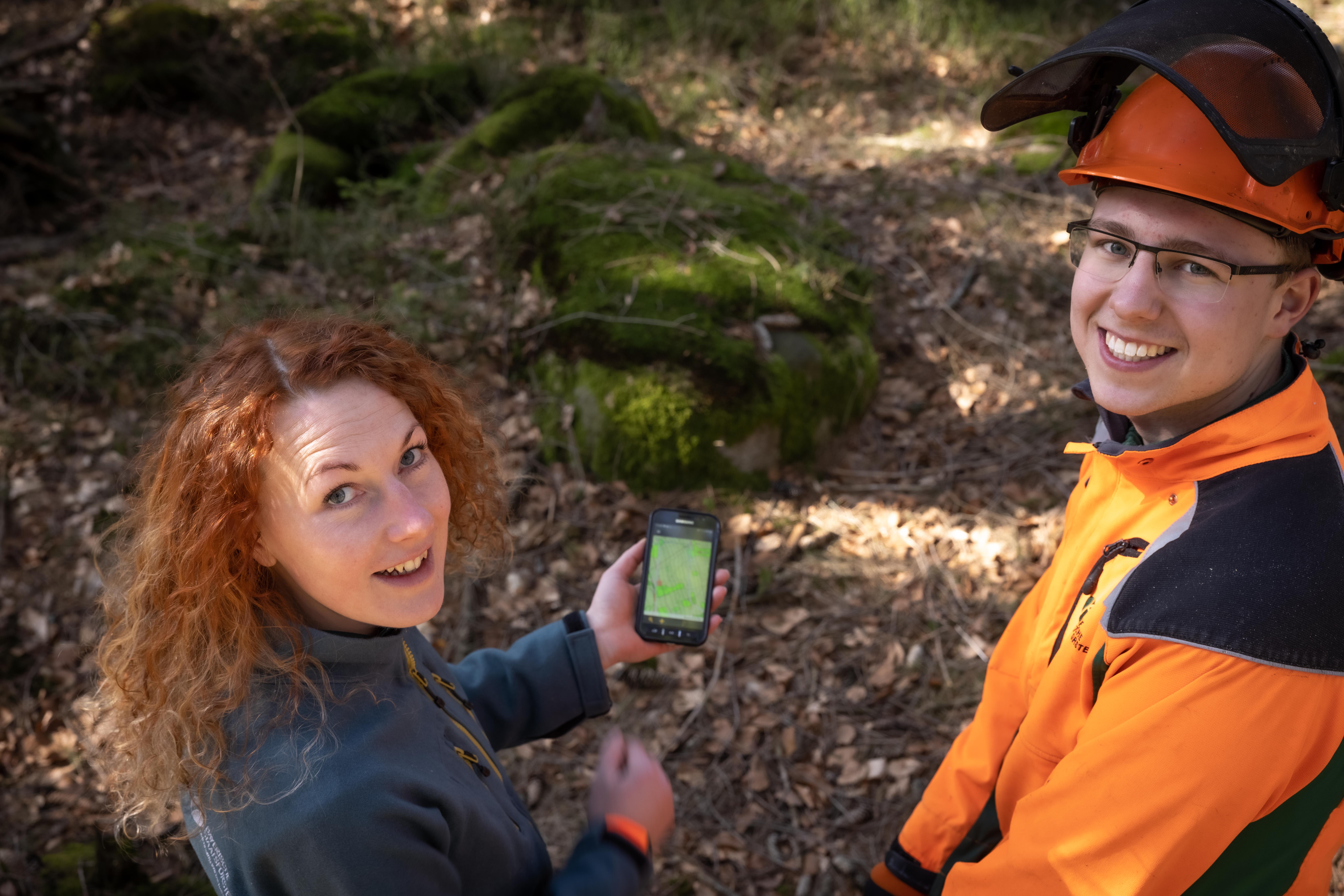 Forstleute schauen in die Kamera, sie haben eine Hand mit einer Waldkarte in der Hand.