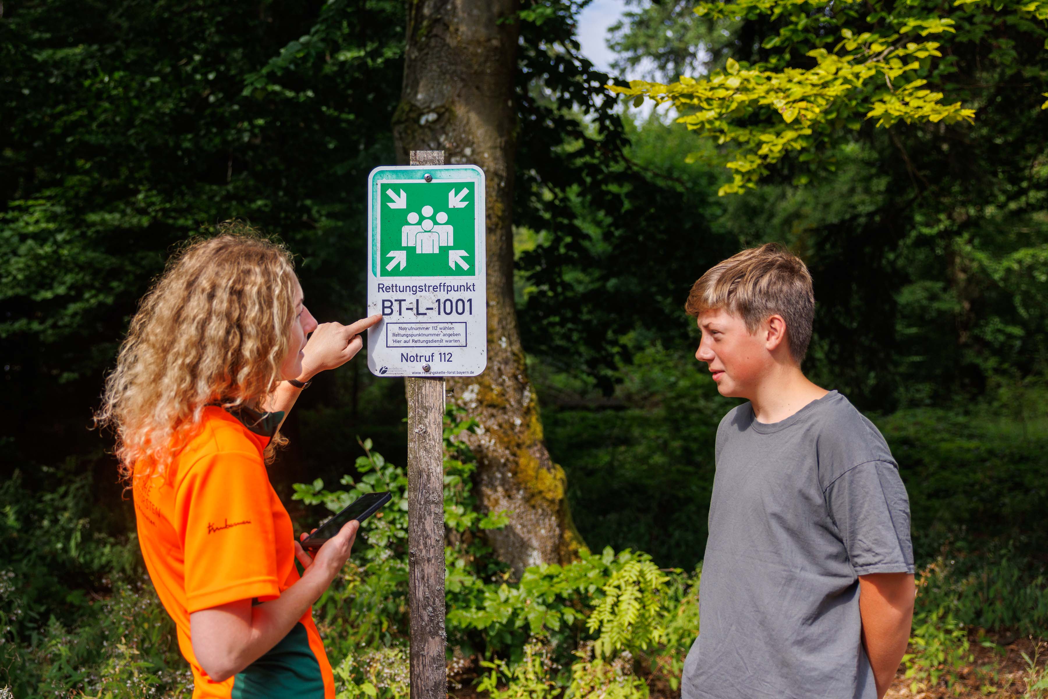 Försterin zeigt auf Schild im Wald, wo Rettungstreffpunkt angeschrieben ist
