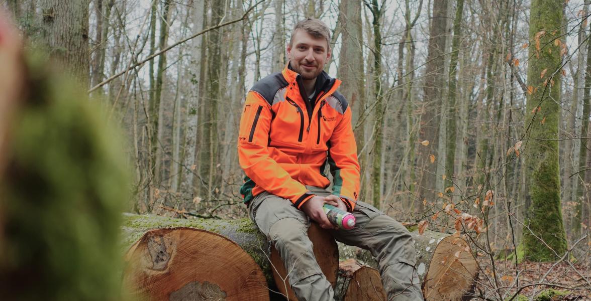 Korbinian Staufer ist neuer Förster im Revier Giesinger Waldhaus in München. Er sitzt auf einem Baumstamm mit einer Spraydose in der Hand