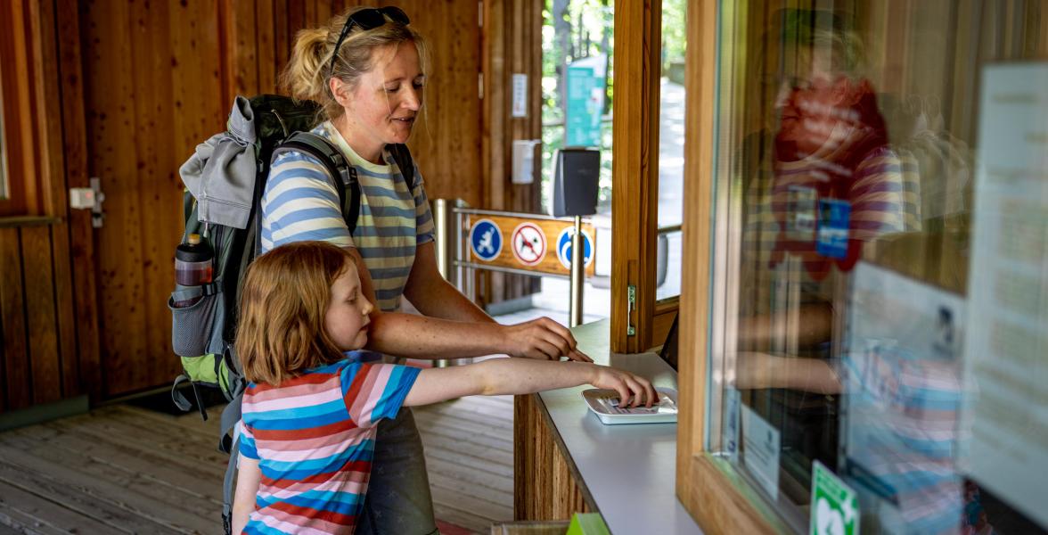 Eine Frau und ein Kind kaufen Tickets für den Baumwipfelpfad Steigerwald