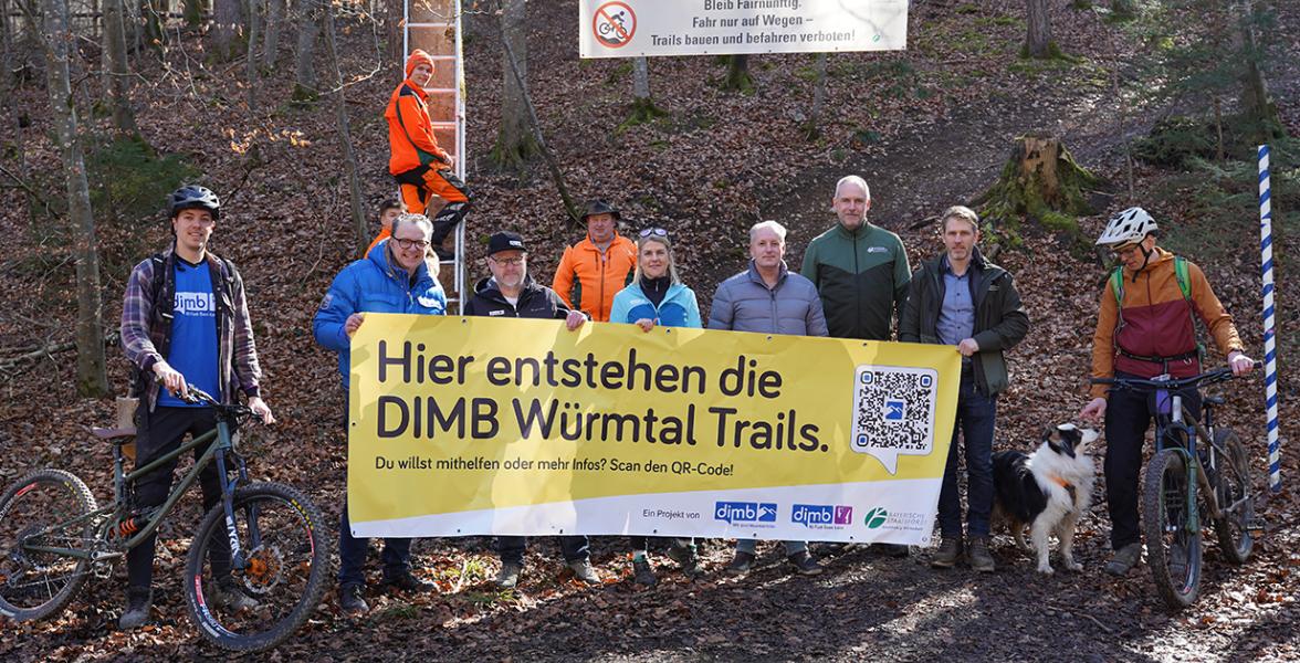 Mitarbeiter des Forstbetriebs und Mountainbiker stehen mit einem Banner, auf dem für die Würmtal-Trails geworben wird, im Wald